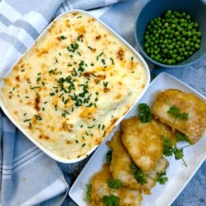A dish of Anglesey eggs next to a plate of lightly battered pieces of fish. There is a bowl of peas in the background.