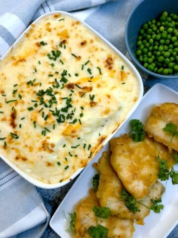 A dish of Anglesey eggs next to a plate of lightly battered pieces of fish. There is a bowl of peas in the background.