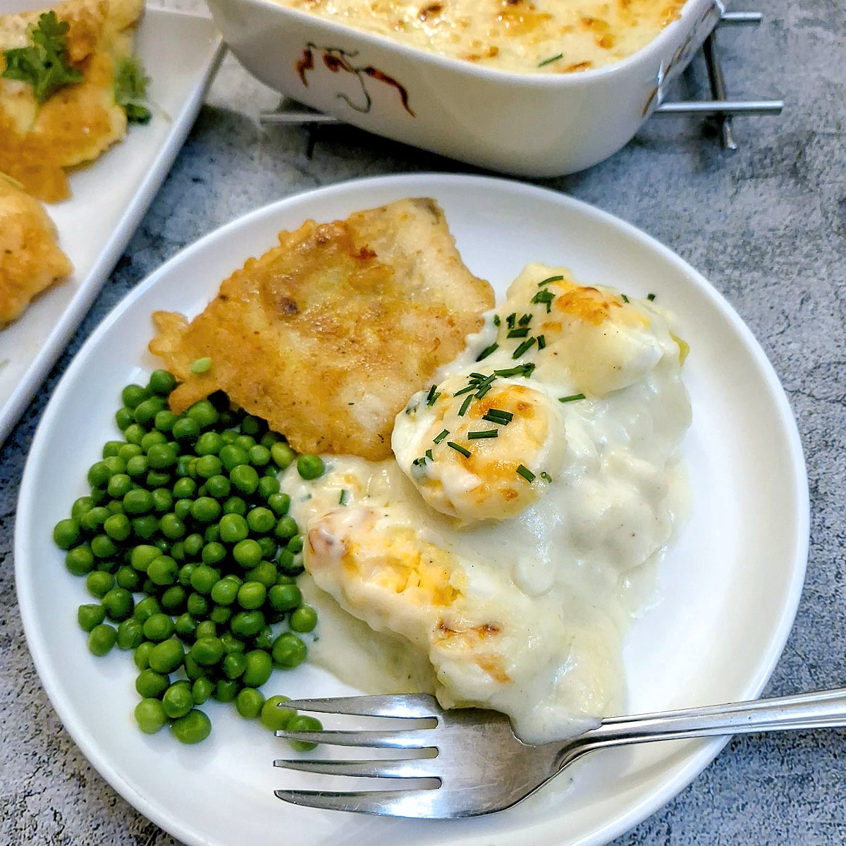 A serving of Anglesey eggs on a plate with a piece of battered fish and a helping of peas.
