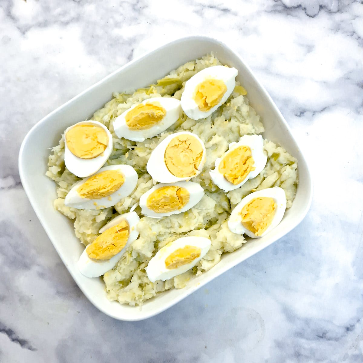 Quartered hard-boiled eggs arranged on leek and potato mash in a baking dish.