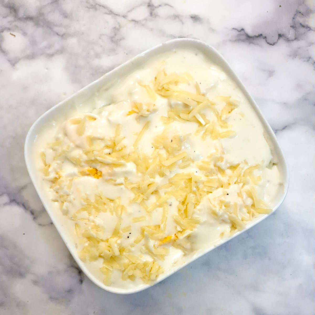An unbaked dish of Anglesey eggs sprinkled with grate cheese.