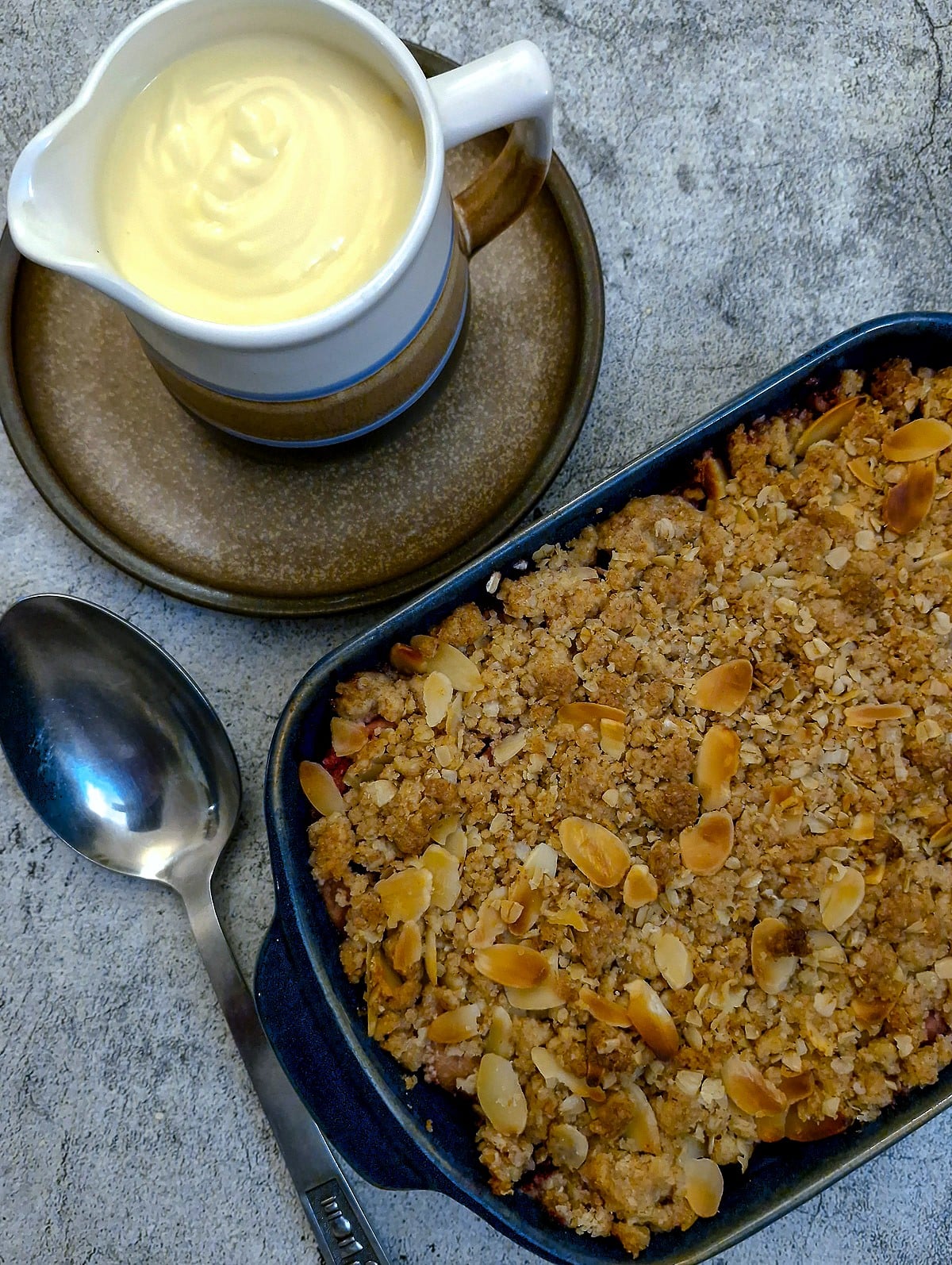 A dsh of apple crumble next to a jug of custard.
