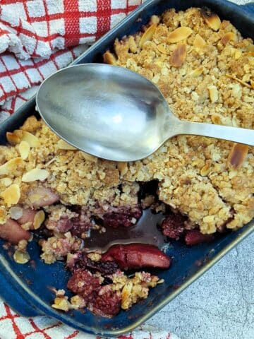Overhead shot of apple and blackberry crumble with one corner removed.