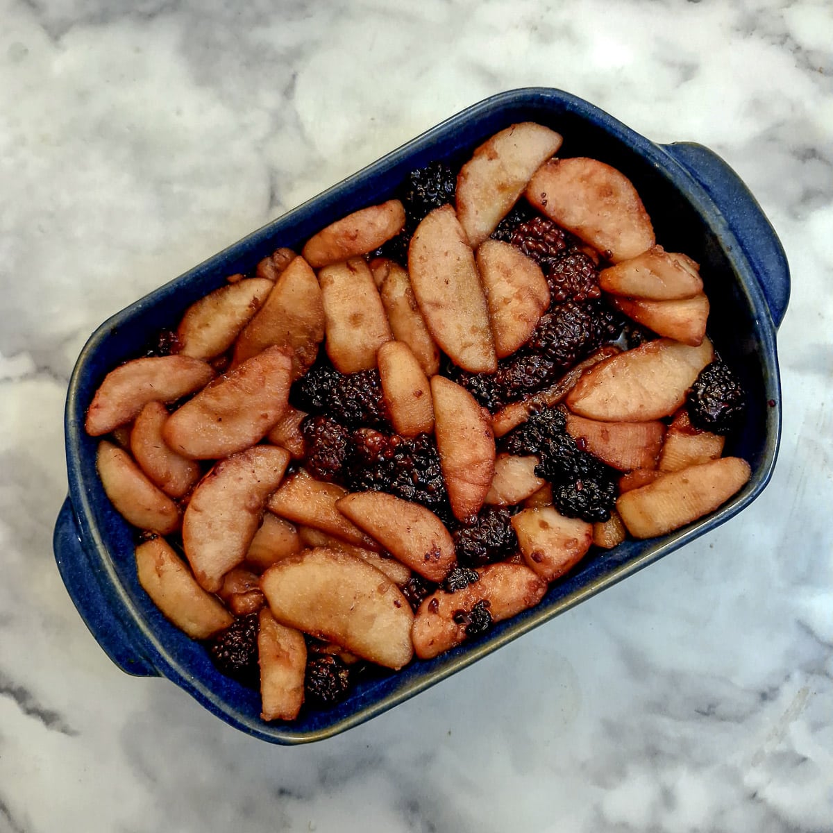 Apples and blackberries in a blue baking dish.