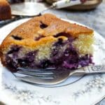 A slice of blueberry sponge cake on a plate with a cake fork.
