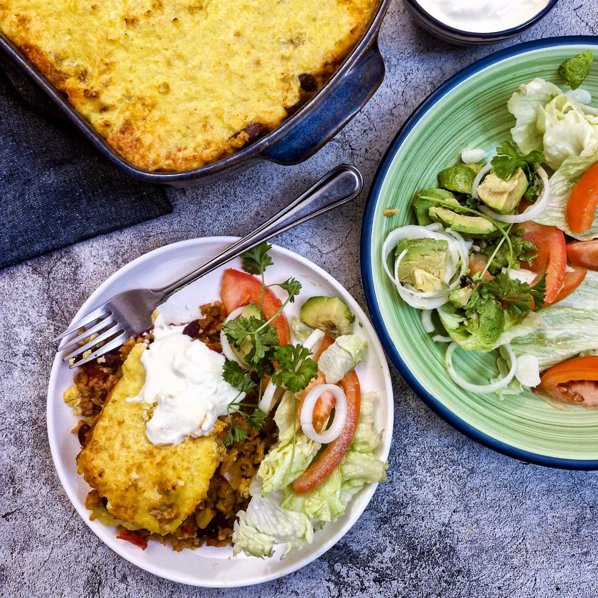 A plate of chilli casserole next to a dish of salad on a table.