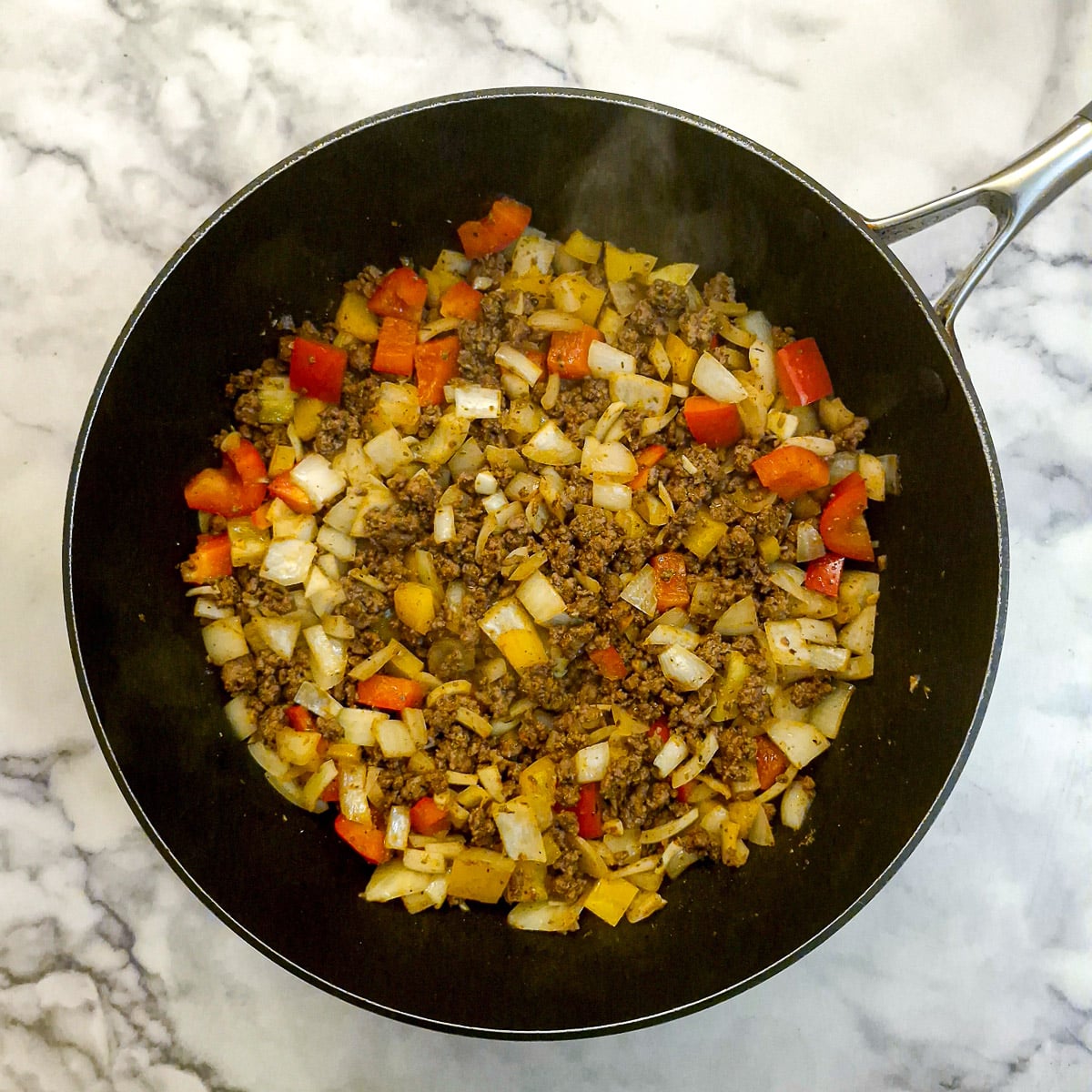 Vegetables softened with ground beef and spices in a frying pan.