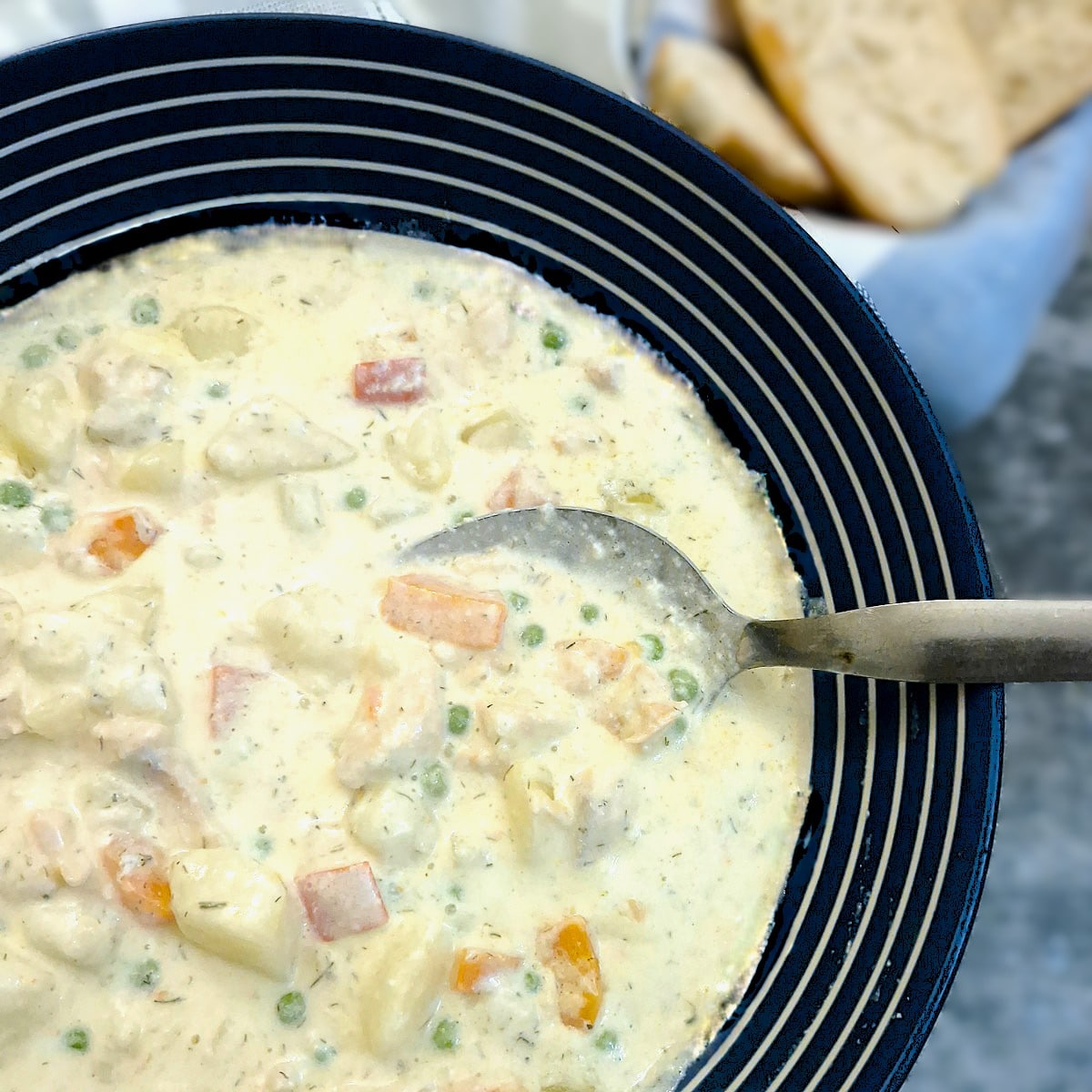 Close up of creamy salmon chowder in a blue and white striped serving dish.