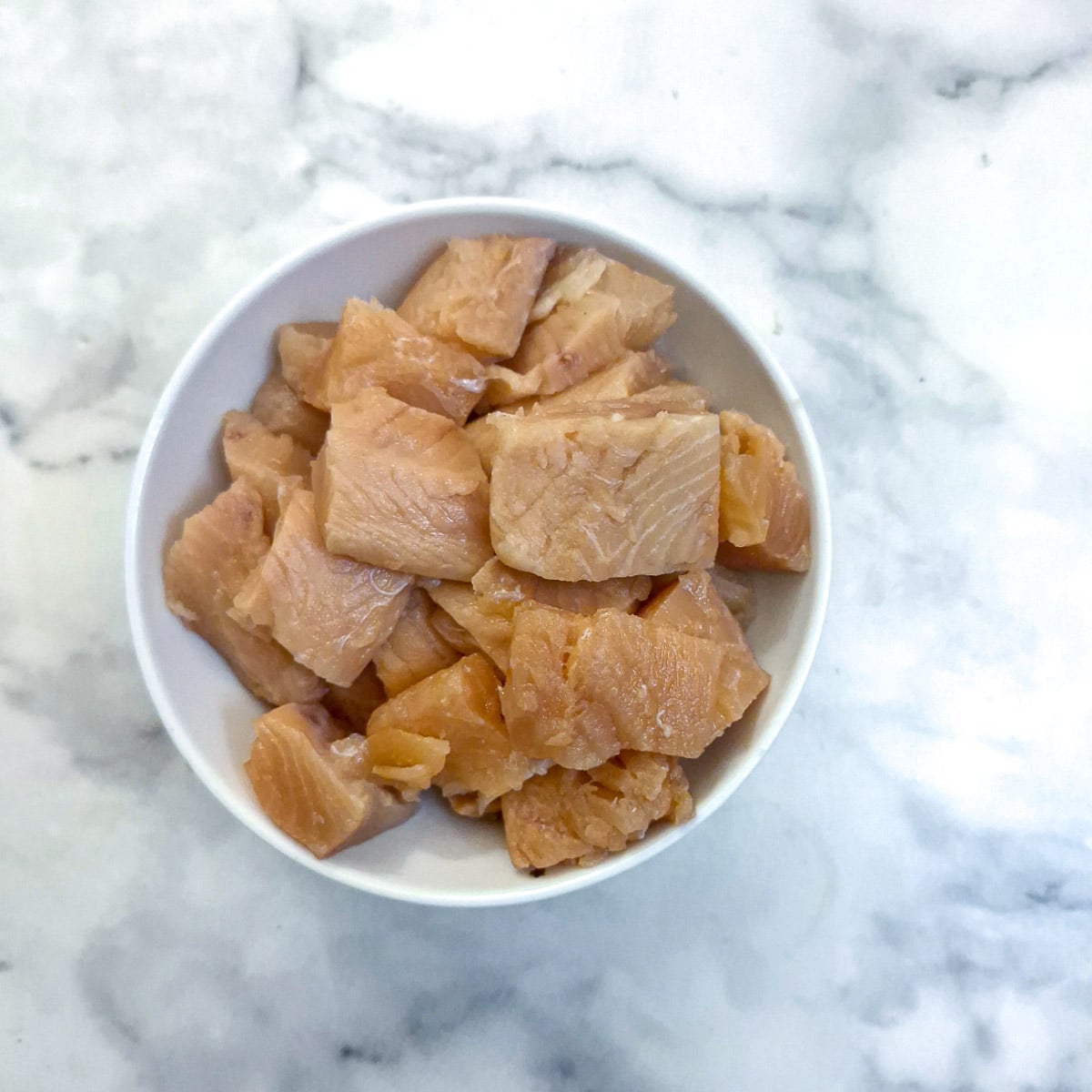 A small white bowl of salmon cut into pieces.