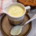 A jug of custard on a brown plate with a spoon.