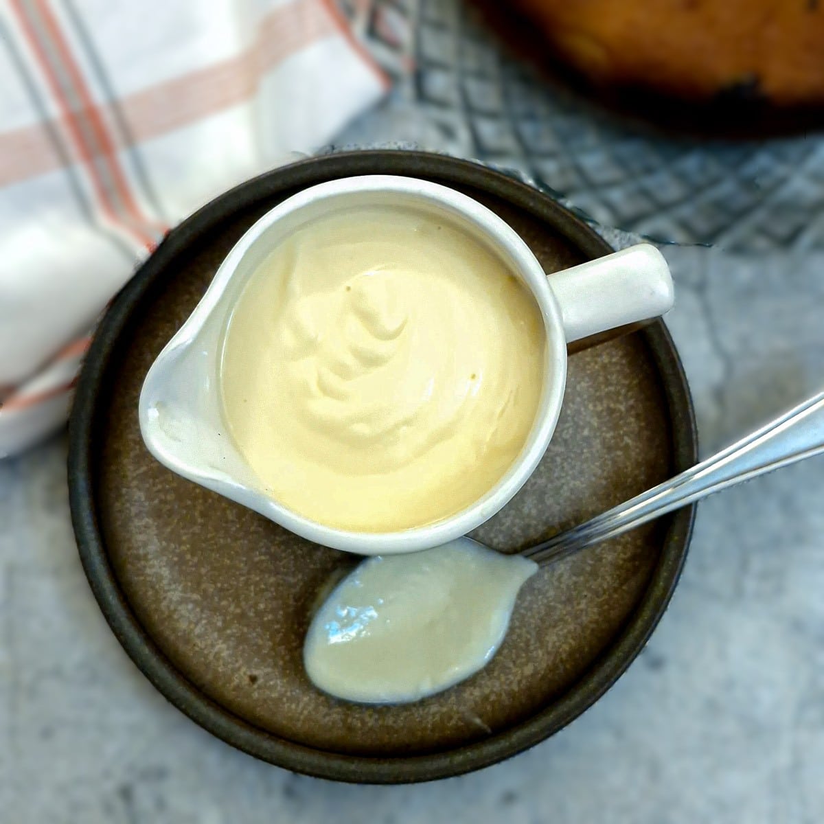 Overhead shot of homemade vanilla custard in a white jug on  brown plate. 