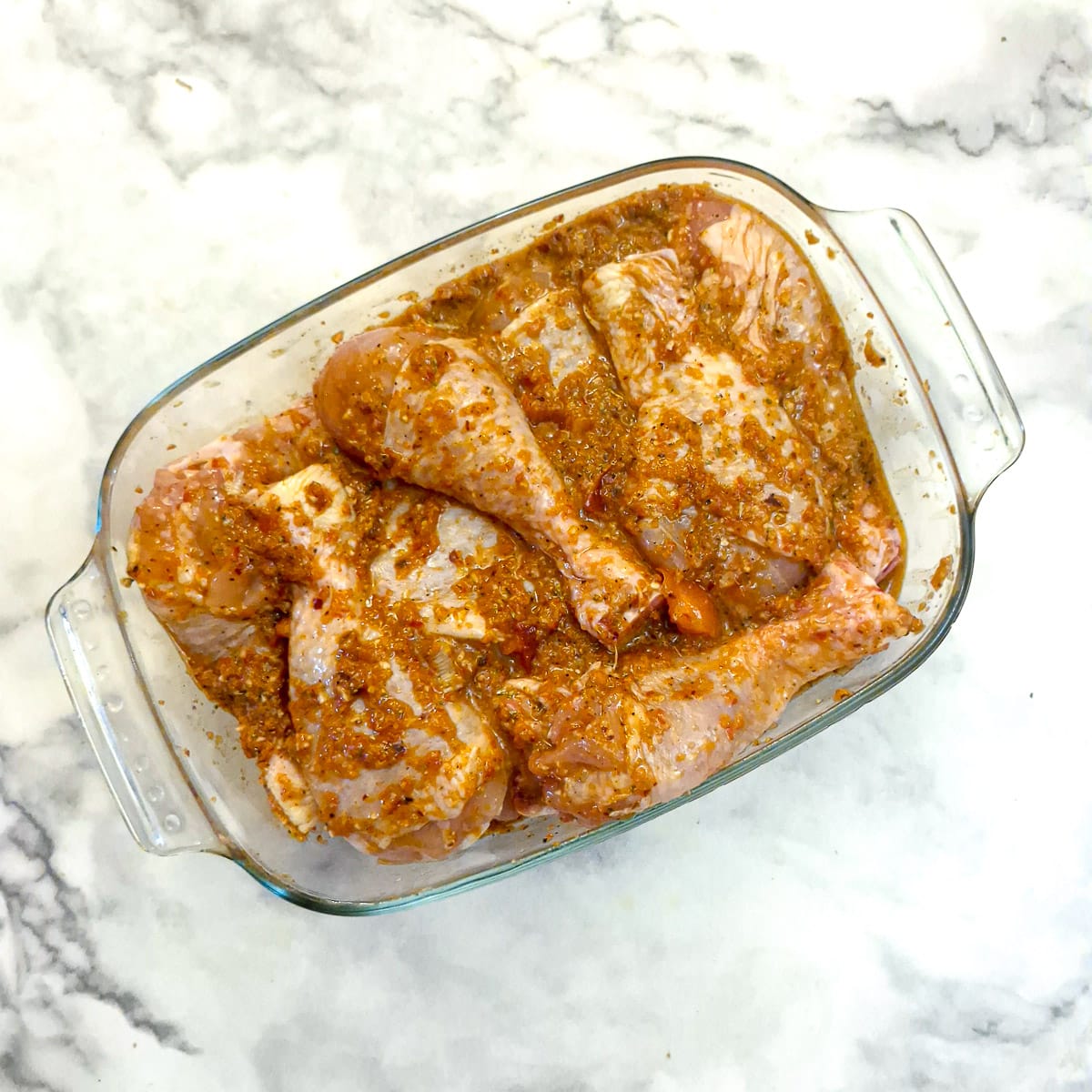 Chicken drumsticks marinating in a rectangular glass dish.