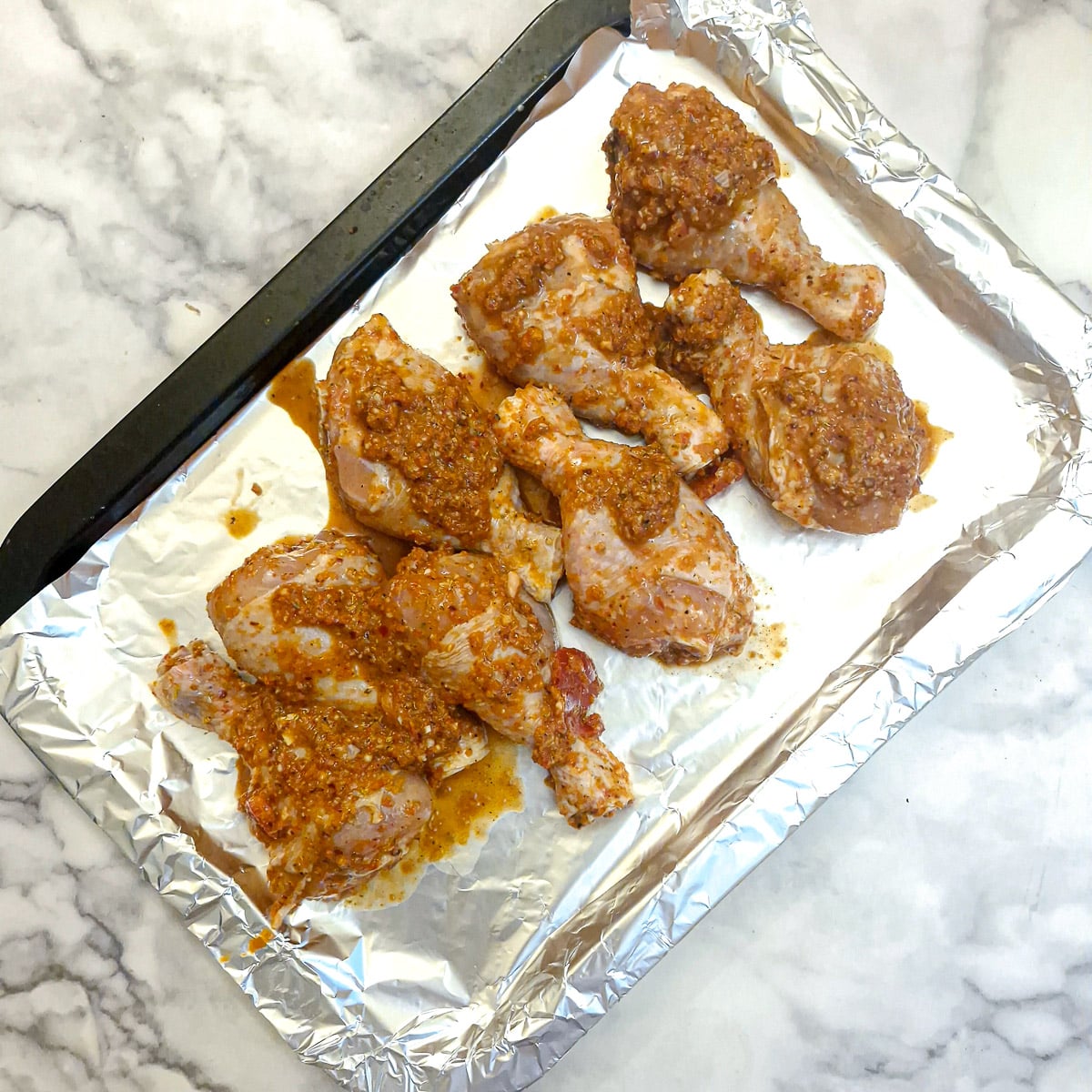 Chicken drumsticks on a foil-lined baking tray.