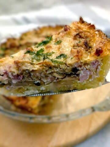 A slice of potato crust bacon and mushroom quiche being lifted from the dish on a cake lifter.