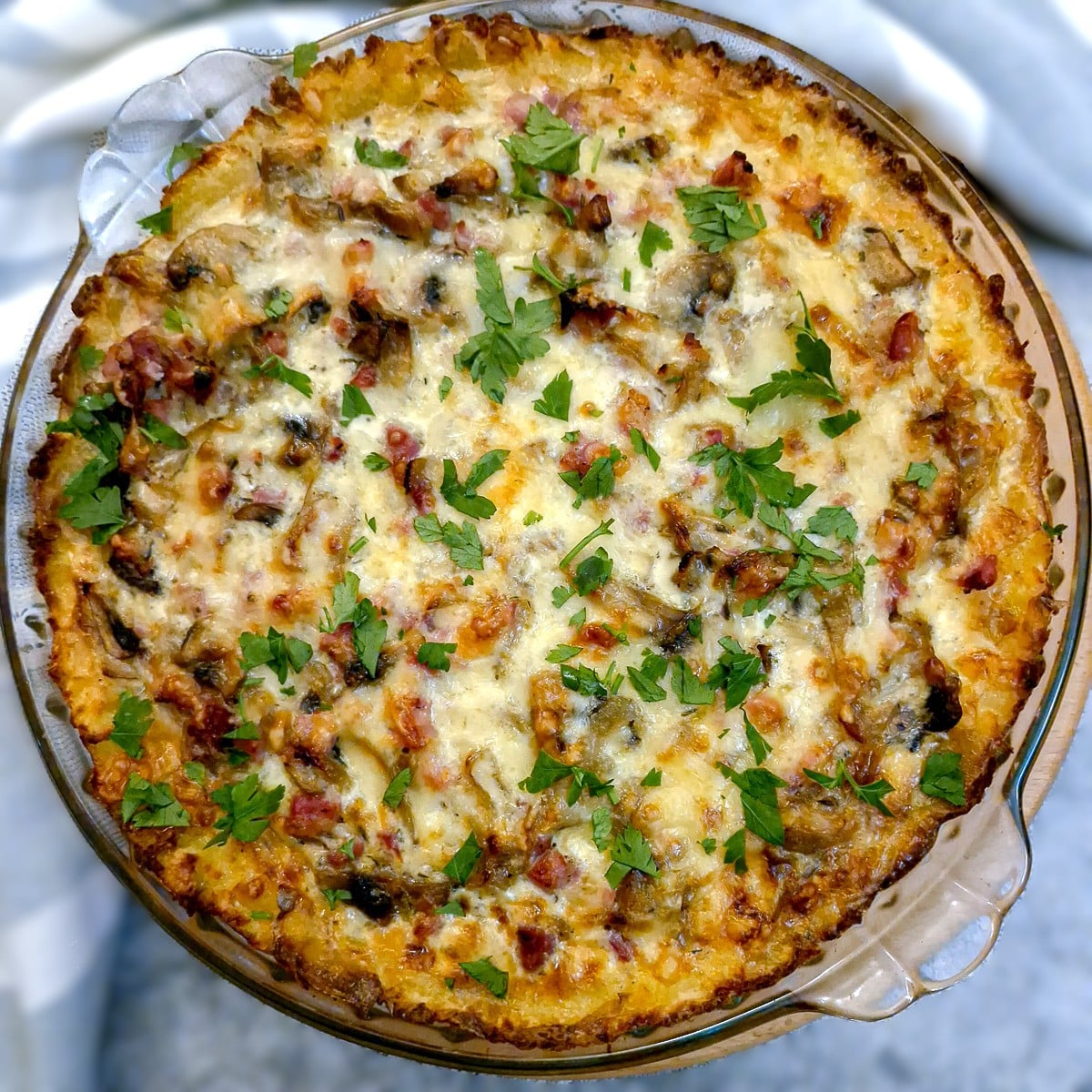 Overhead shot of a potato crust bacon and mushroom quiche in a round baking dish.