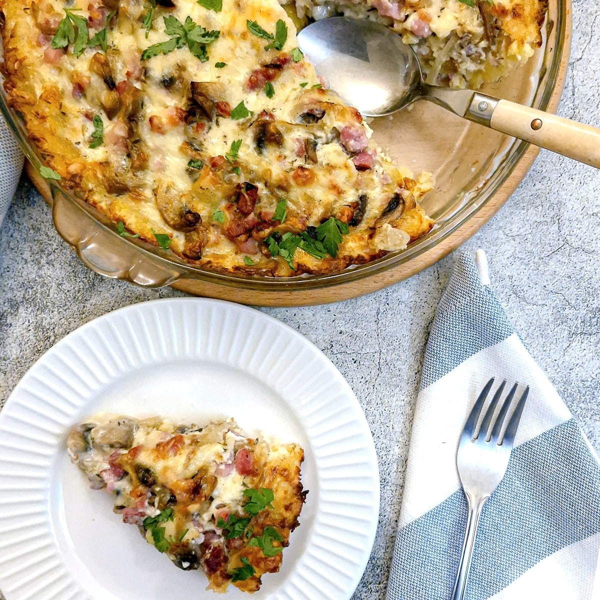 A slice of bacon and mushroom quiche on a plate with the quiche in a baking dish in the background.
