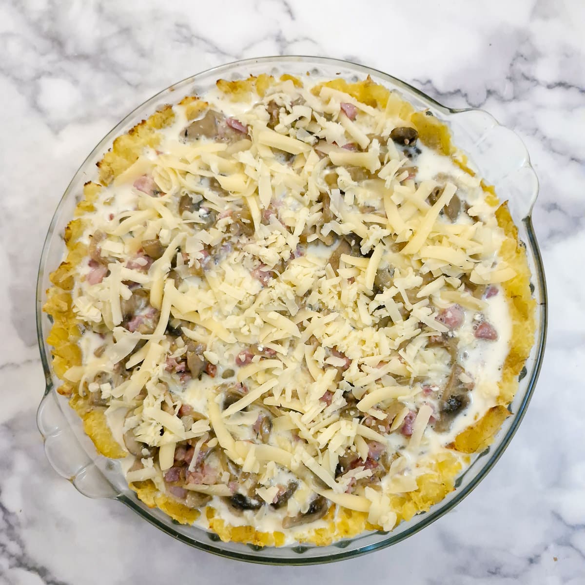 An unbaked bacon and mushroom quiche sprinkled with grate cheese, ready for the oven.