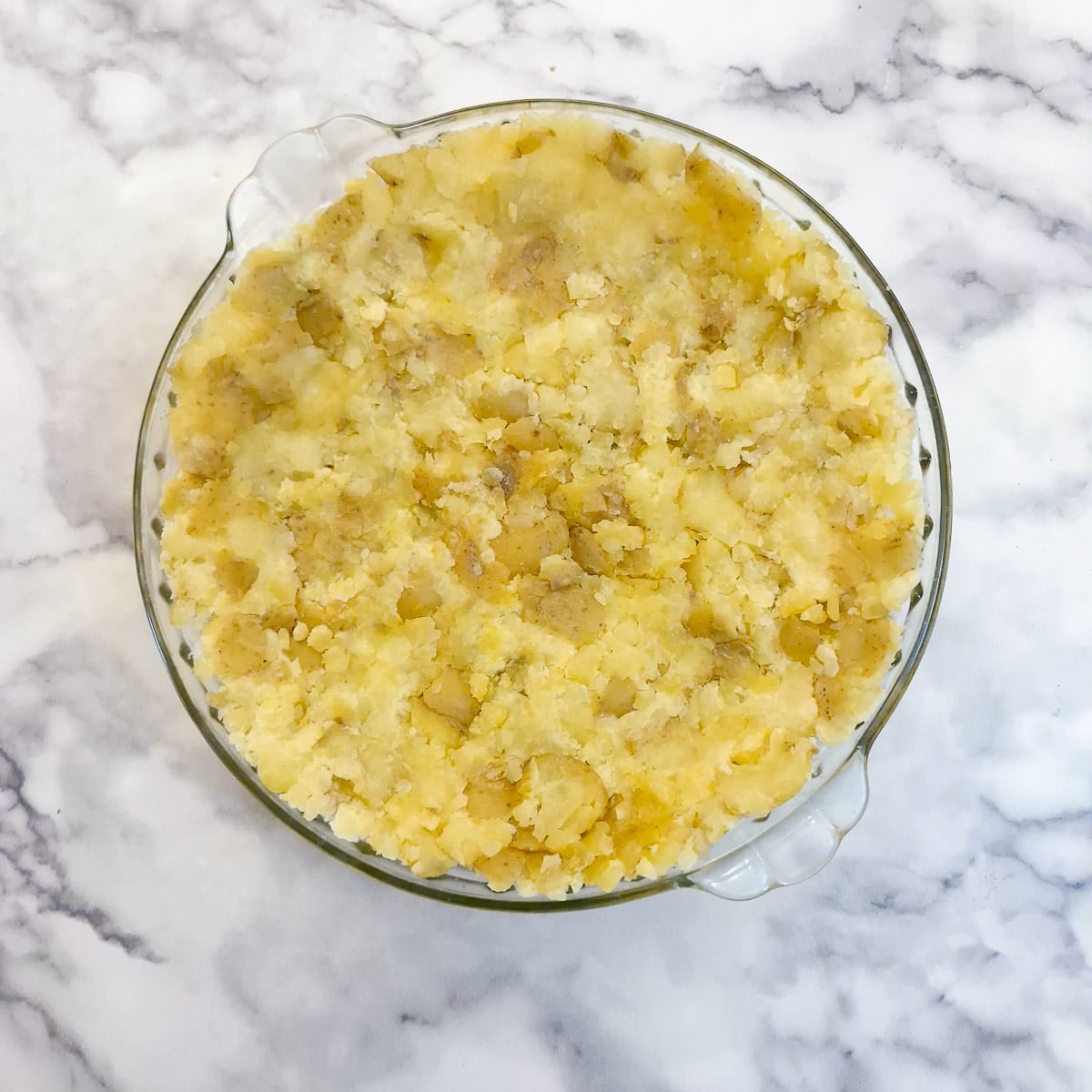 Crushed potatoes pressed into a baking dish to form a pie crust.