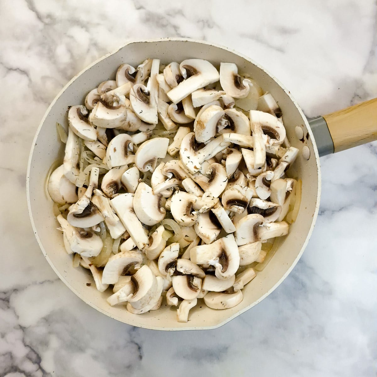 Chopped mushrooms added to the onions in a frying pan.