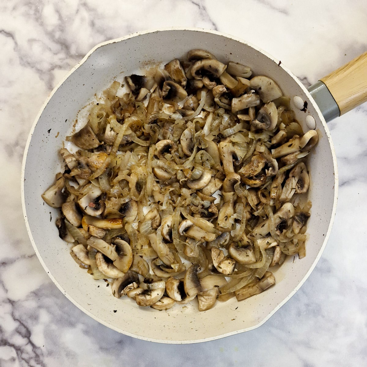 Cooked onions and mushrooms in a frying pan.