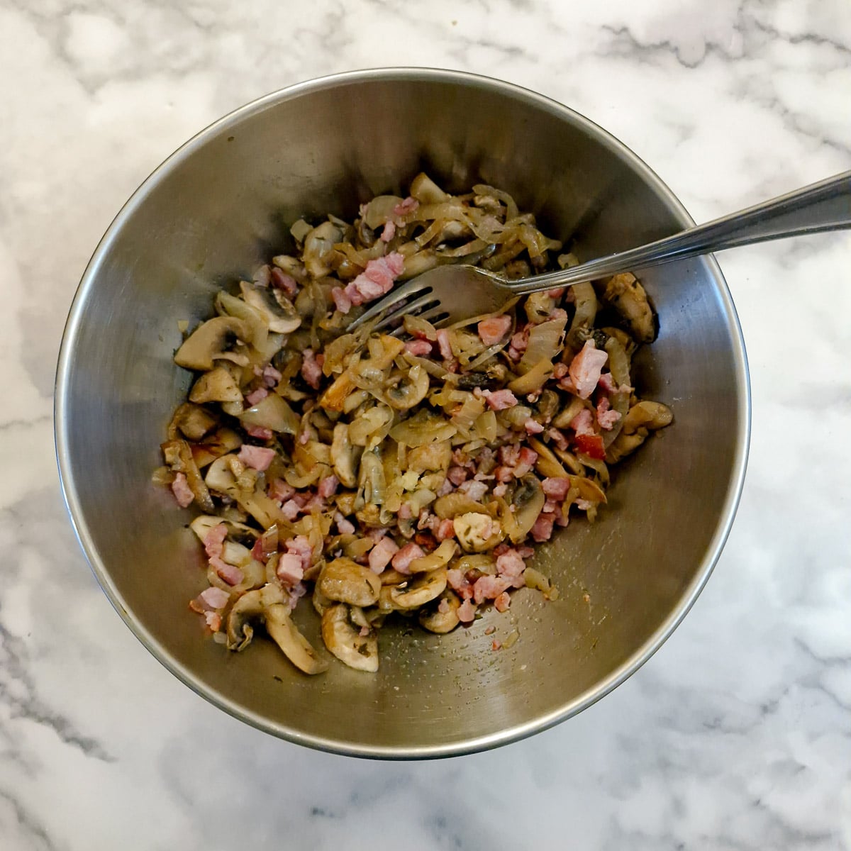 Cooked bacon lardons, mushrooms and onions combined in a mixing bowl.