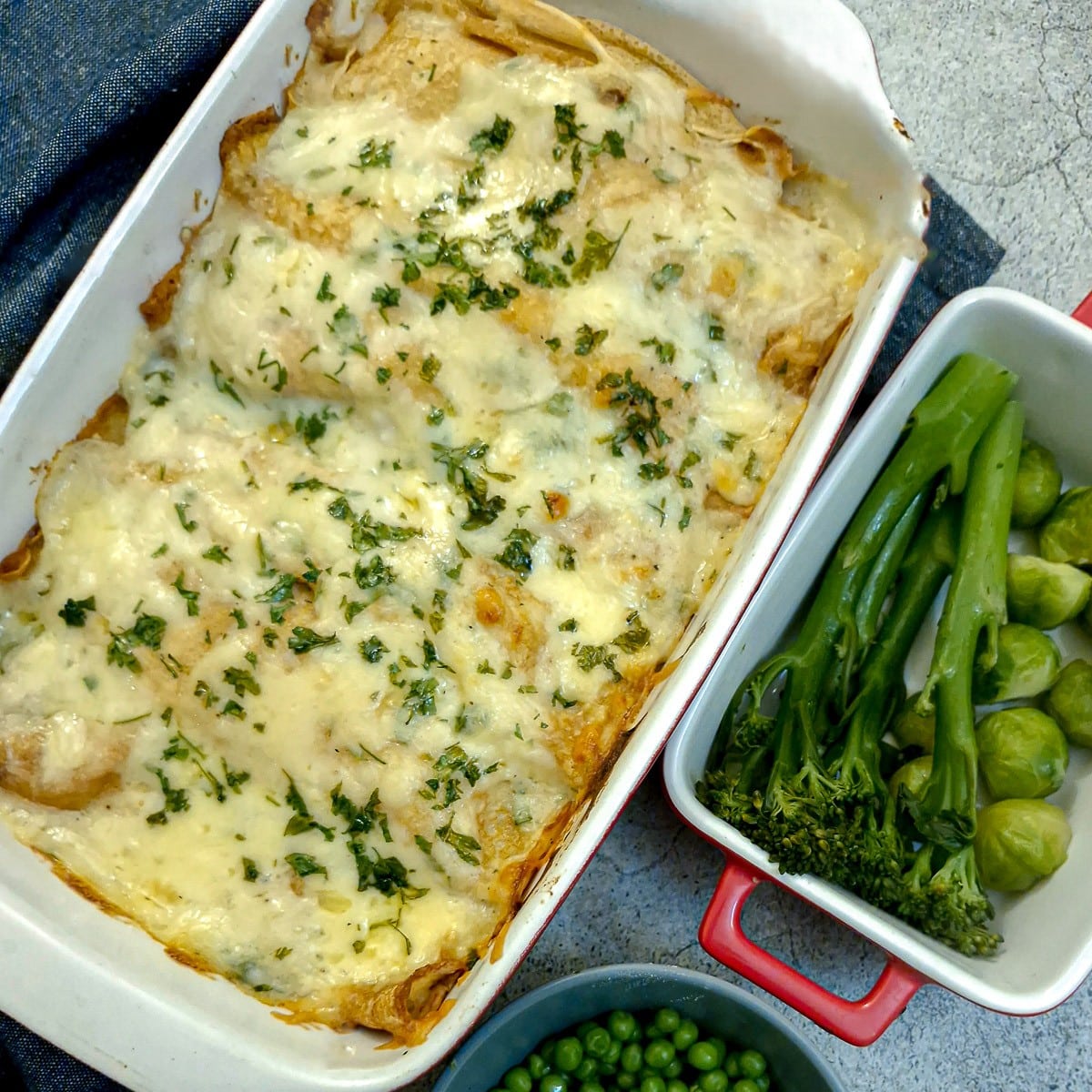 A dish of seafood-stuffed pancakes covered in cheese sauce and garnished with parsley.