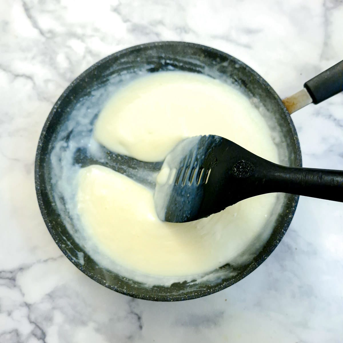 Cheese sauce in a frying pan with a spatula being pulled through to leave a trail.
