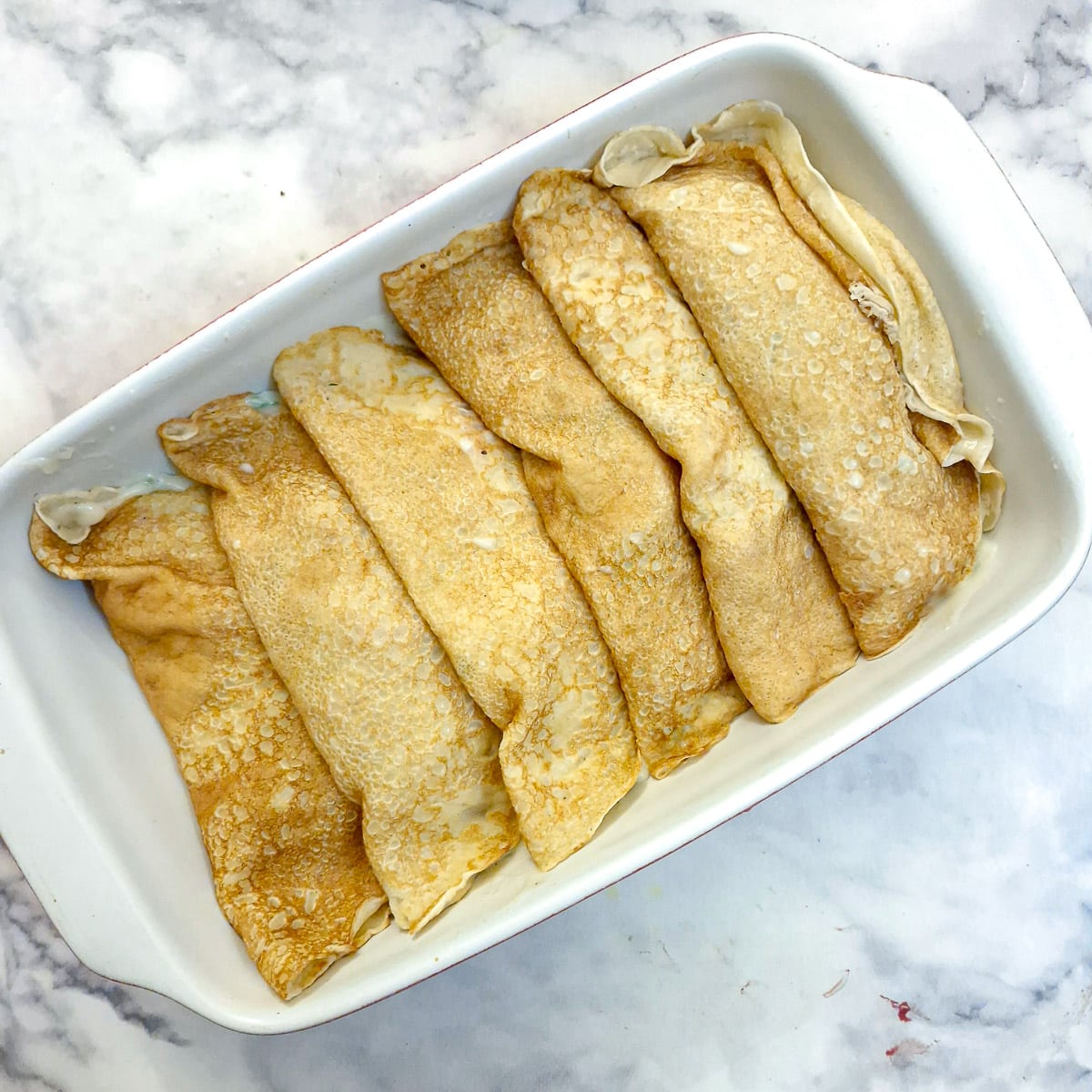 6 stuffed pancakes in a baking dish.