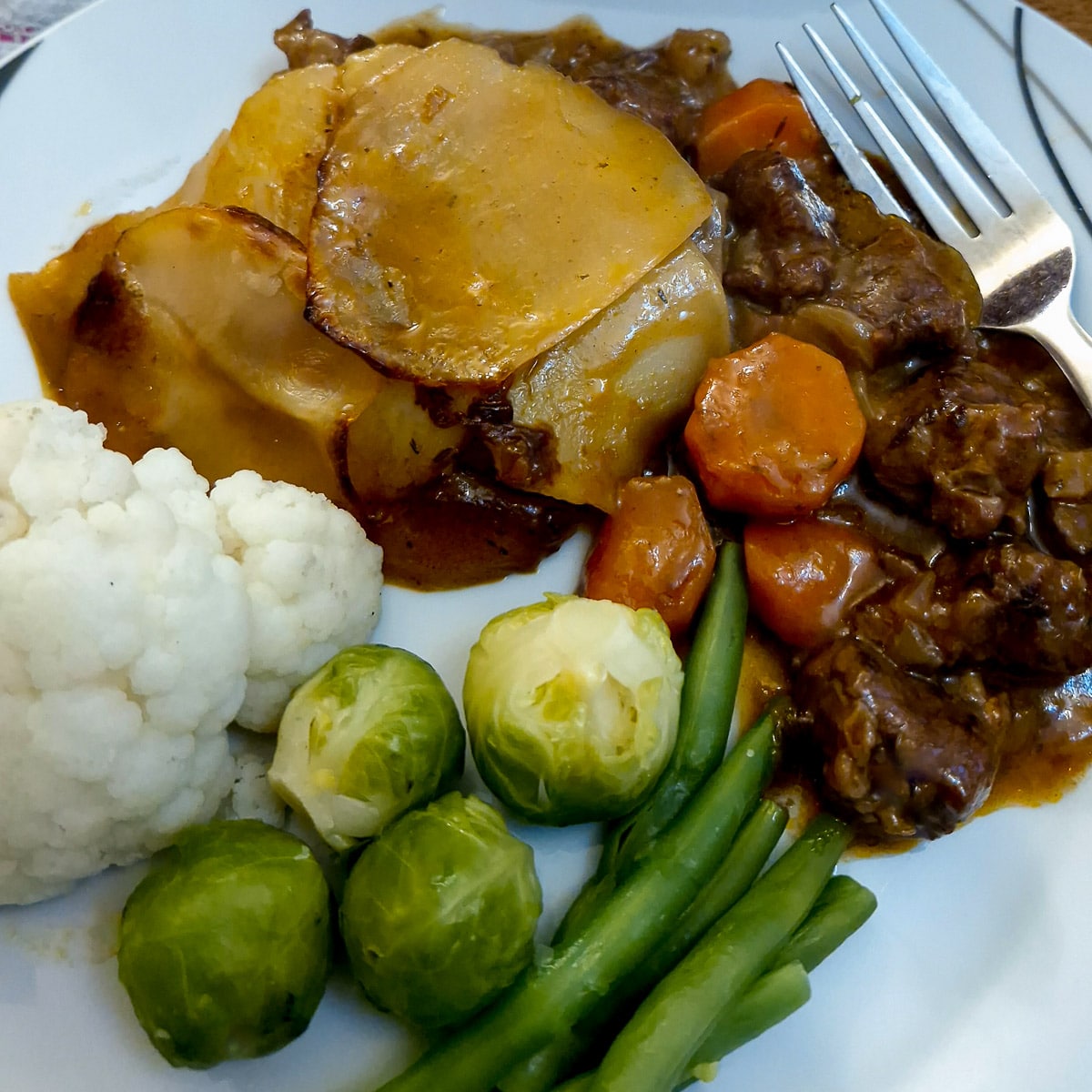 A plate of steak and kidney hotpot with steamed vegetables.