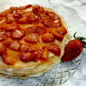 A strawberry custard pancake cake on a glass plate with a large strawberry.