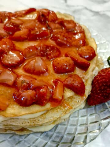 A strawberry custard pancake cake on a glass plate with a large strawberry.