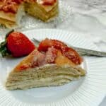 A slice of strawberry custard pancake cake on white plate with a large strawberry on the side.