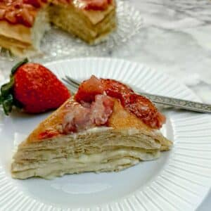 A slice of strawberry custard pancake cake on white plate with a large strawberry on the side.
