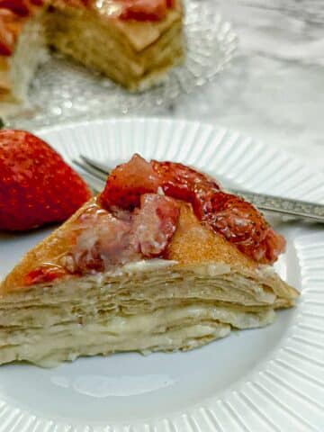 A slice of strawberry custard pancake cake on white plate with a large strawberry on the side.