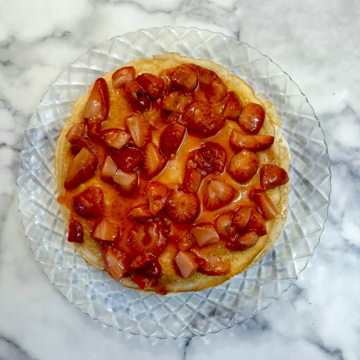 Strawberry compote poured on top of a pile of pancakes and custard.
