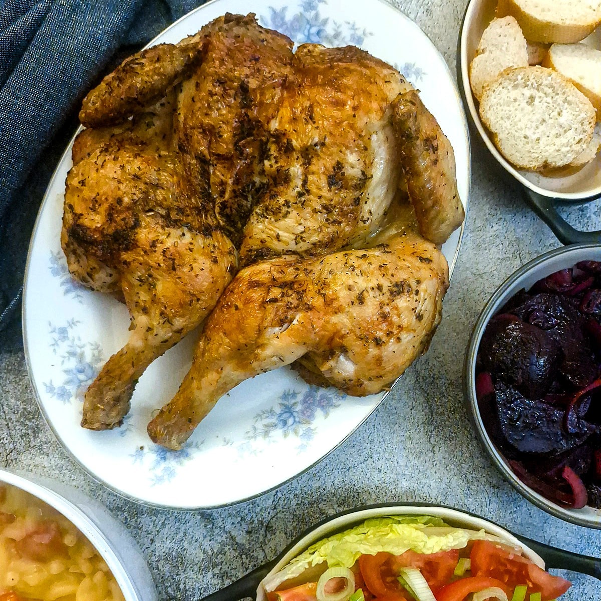 A lemon and herb chicken flattie on a serving plate surrounded by dishes of salad.