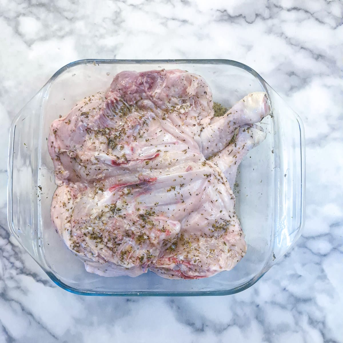 A flattened chicken laying skin-side down in marinade in a glass bowl.