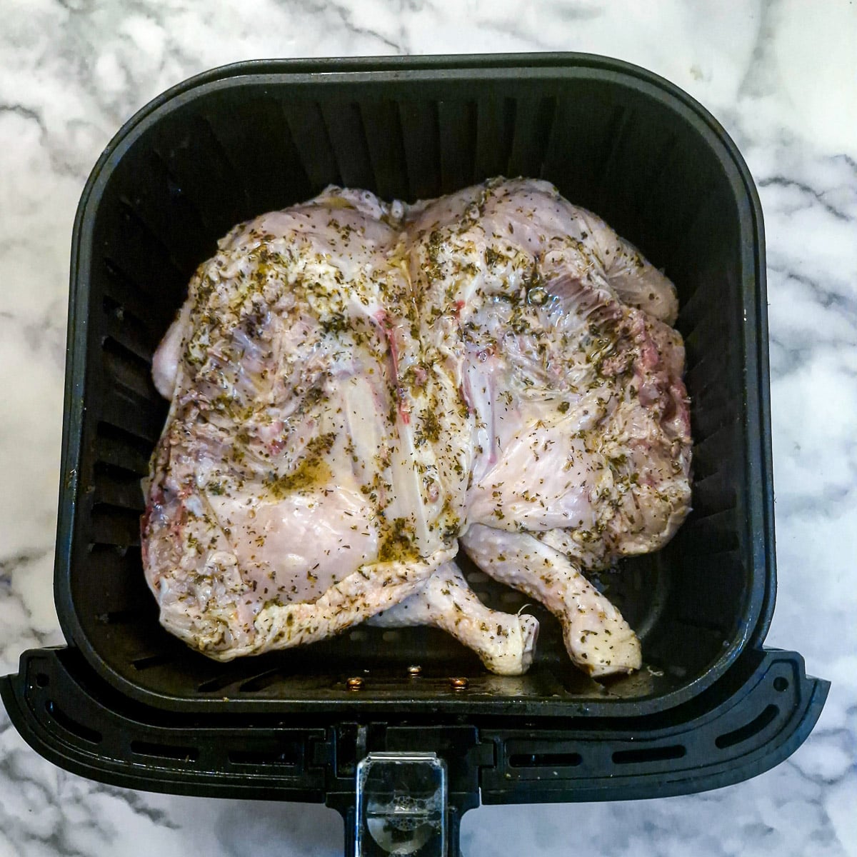 A marinated chicken laying skin-side down in an an air fryer basket.