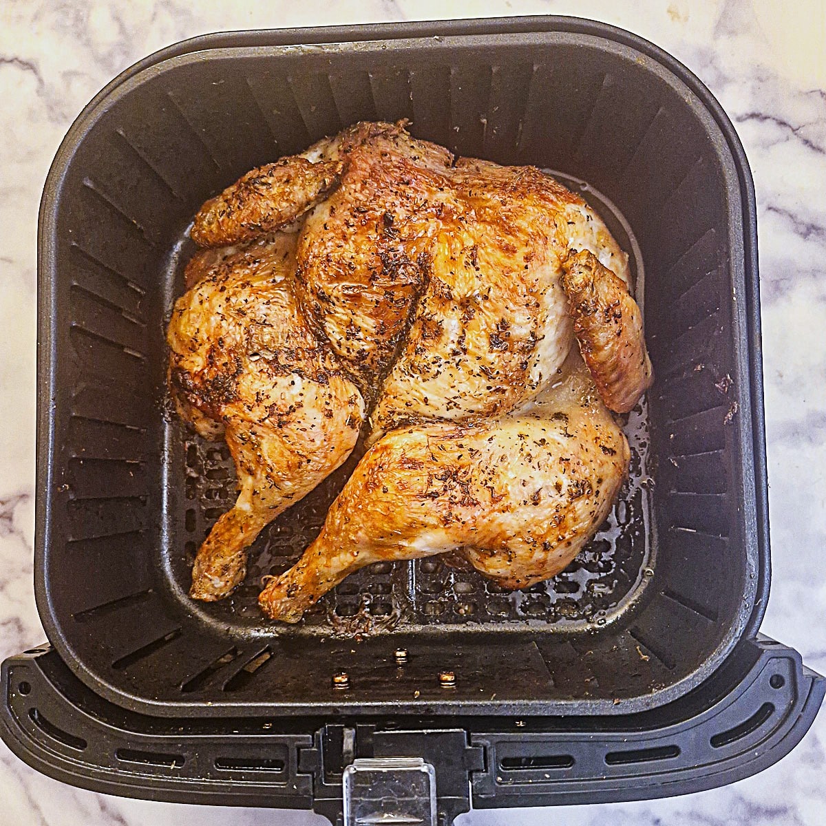 A golden brown skinned cooked chicken in an air fryer basket.