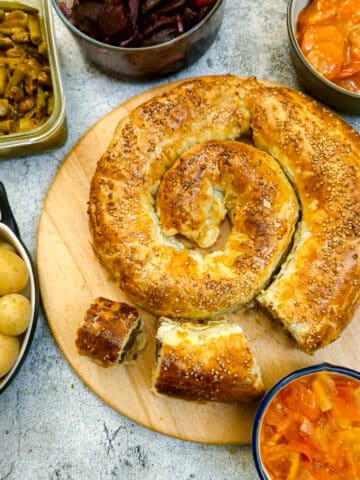 A boerewors puff pastry spiral on a wooden board surrounded by a selection of salads.