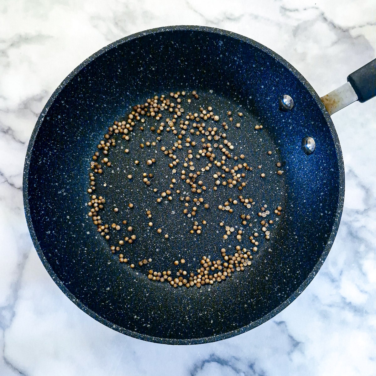 Coriander seeds in a dry frying pan.