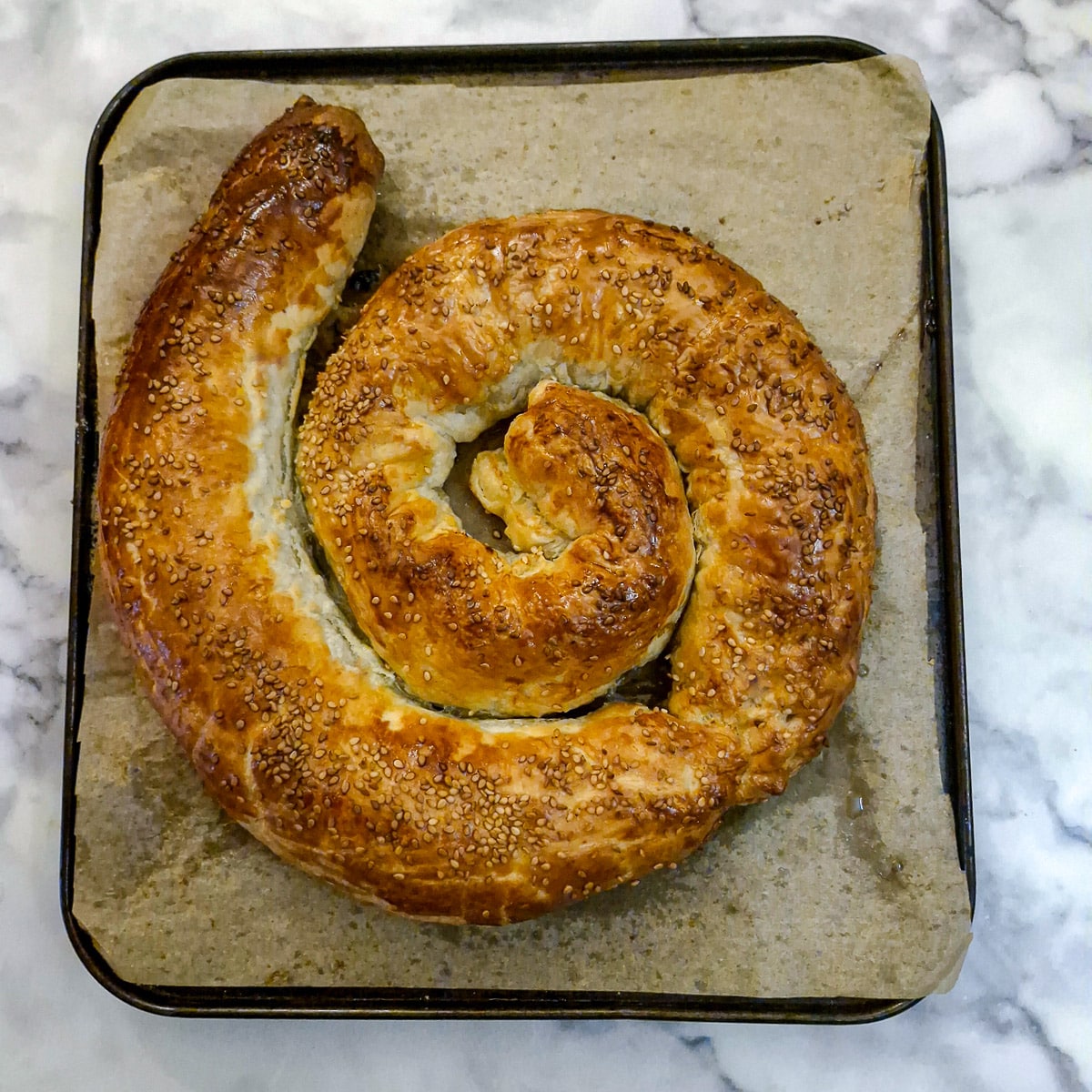 A golden brown crispy boerewors puff pastry spiral on a baking 
tray.