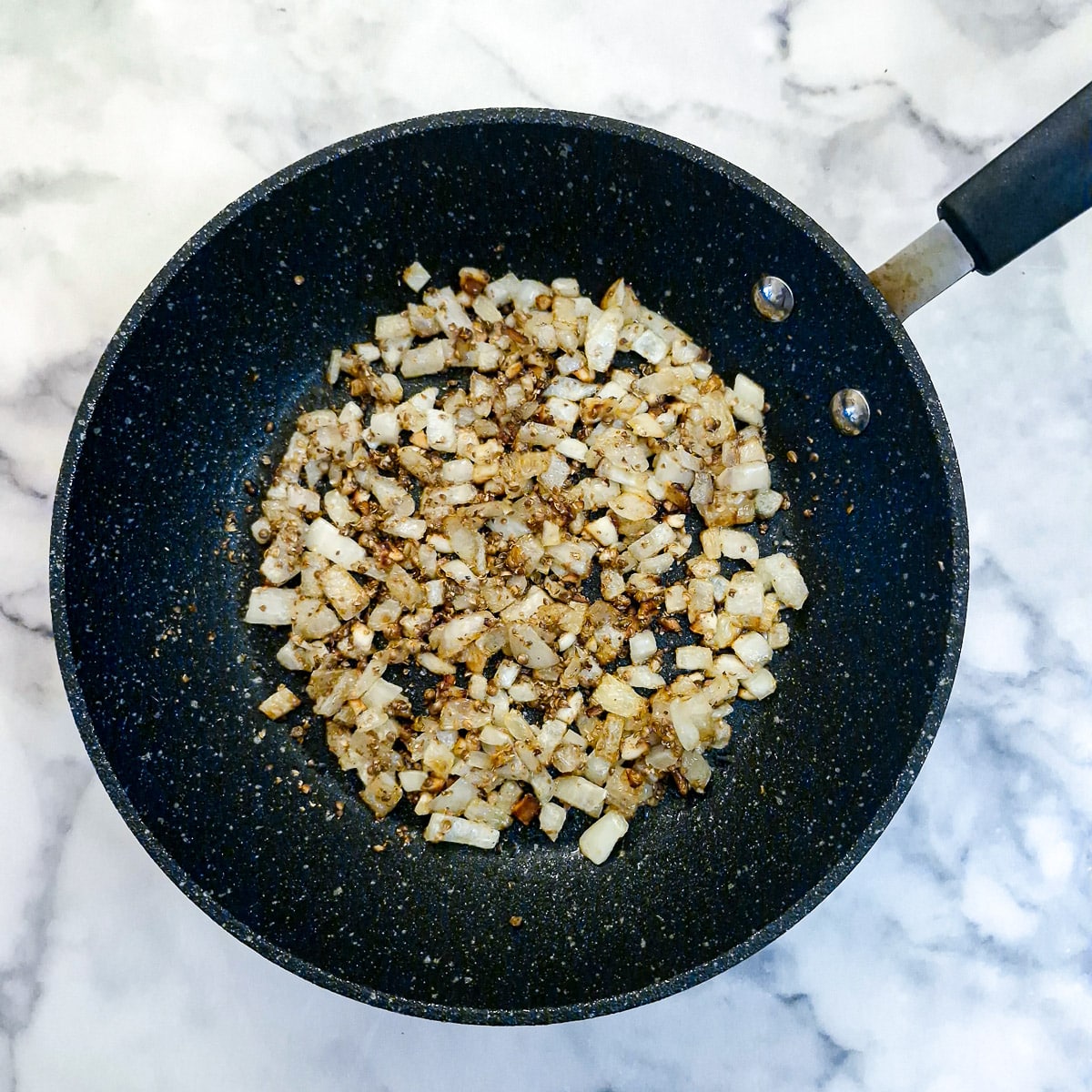 Onions and crushed coriander seeds in a frying pan.