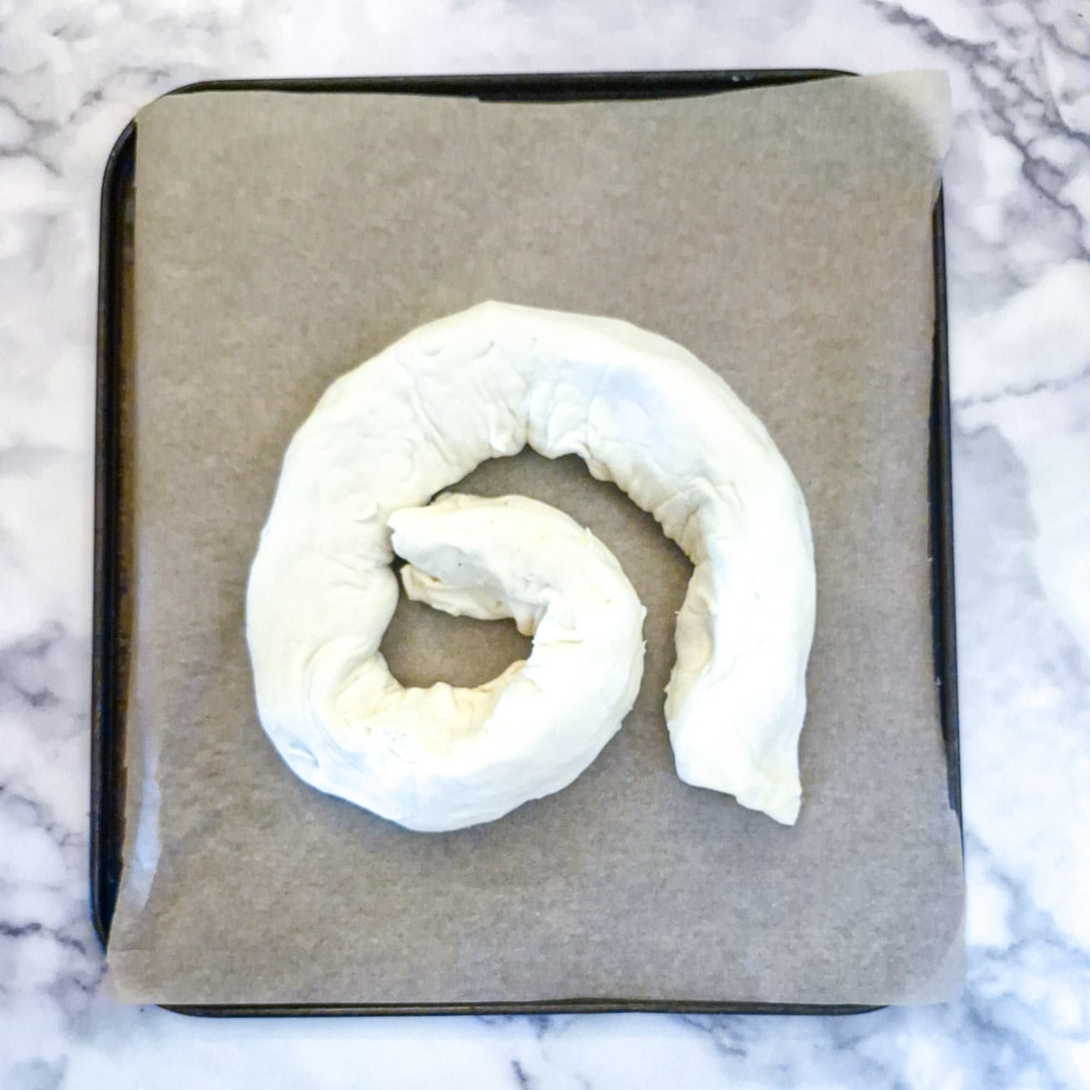 One half of the puff pastry and boerewors meat formed into a coil on a baking sheet.