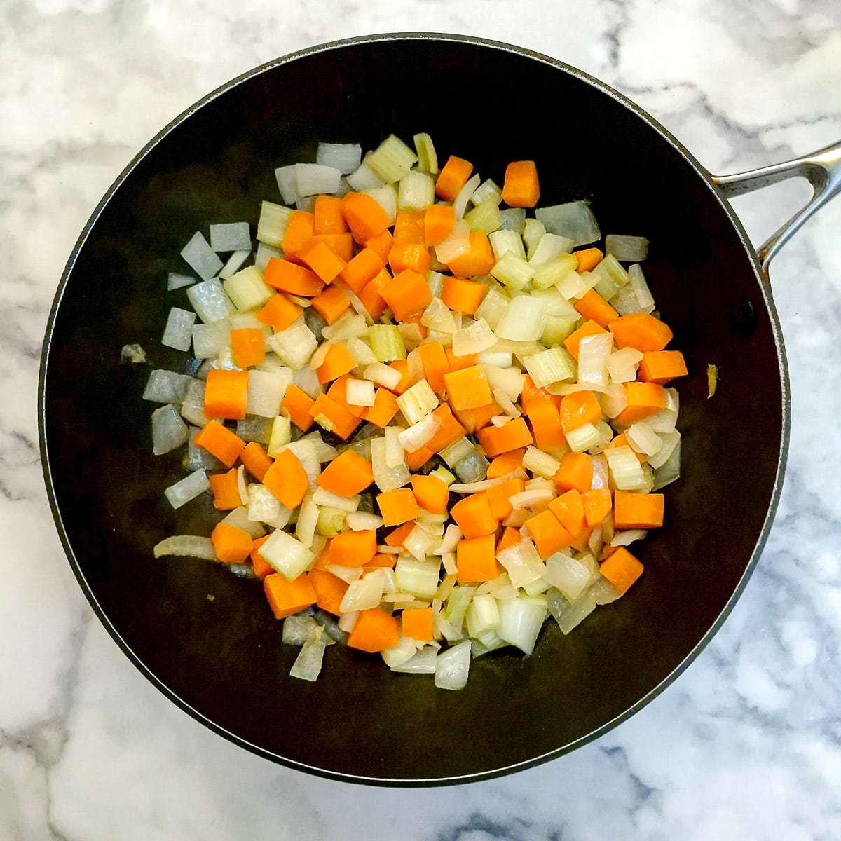 Carrots, onions and celery softening in a frying pan.
