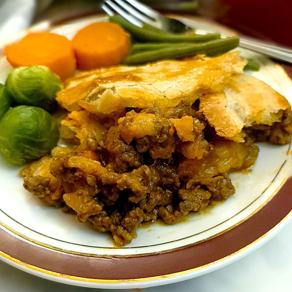 A slice of minced meat pie on a plate with steamed vegetables.