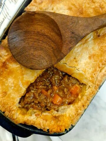 An easy meat pie in a baking dish with a corner of the pastry removed to show the filling.