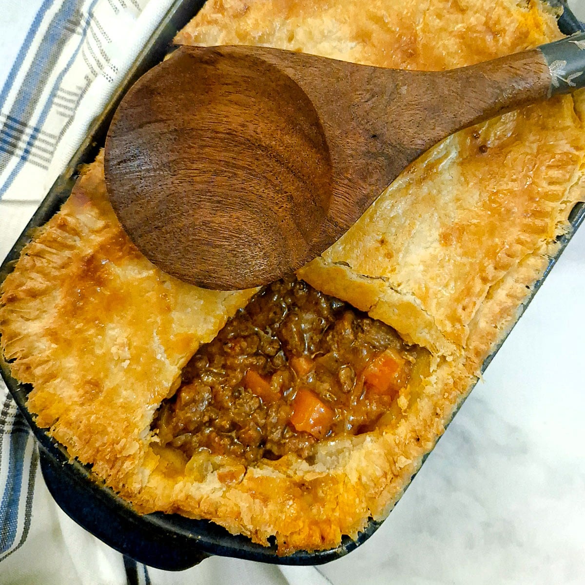 An easy meat pie in a baking dish with a corner of the pastry removed to show the filling.