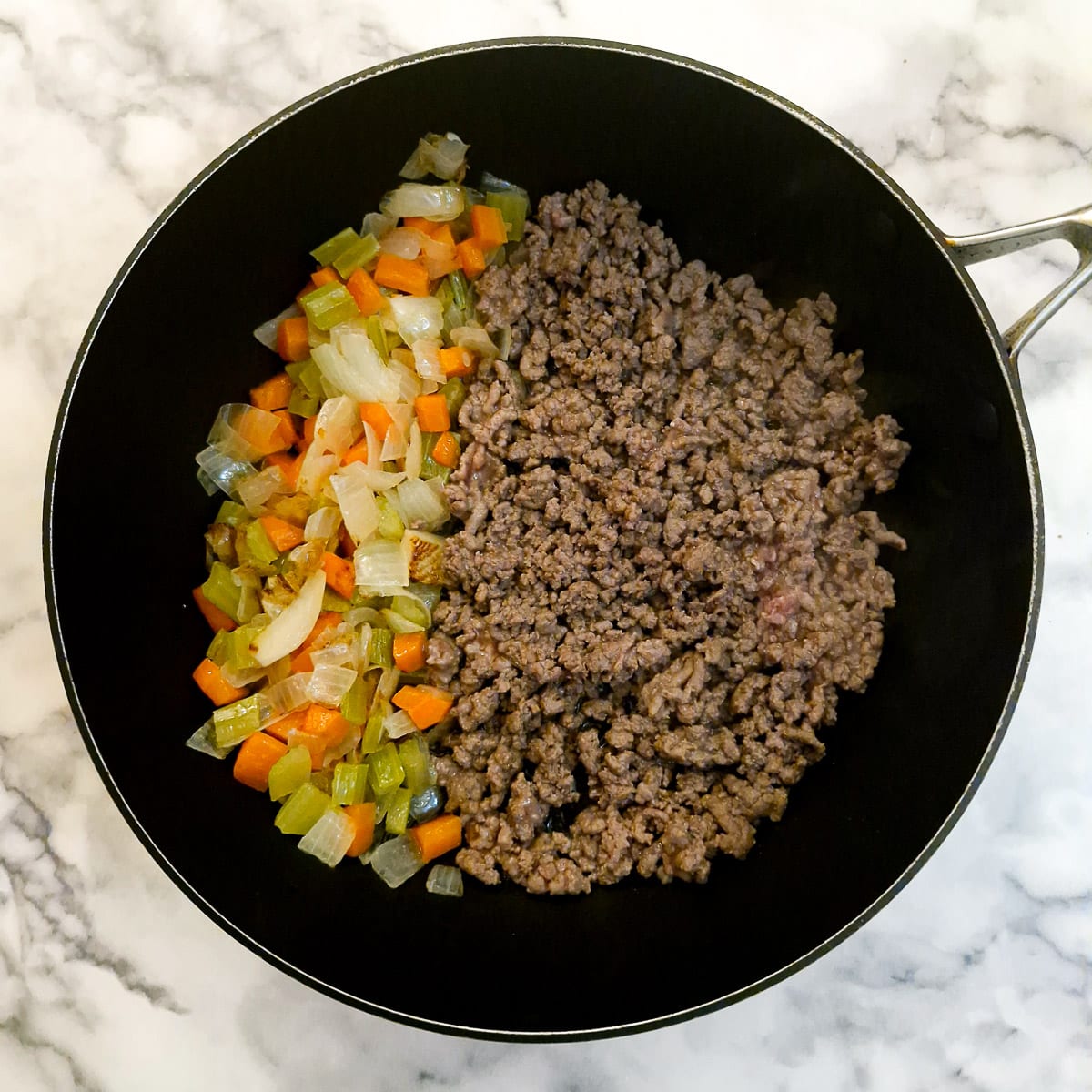 Ground beef browning with vegetables in a frying pan.