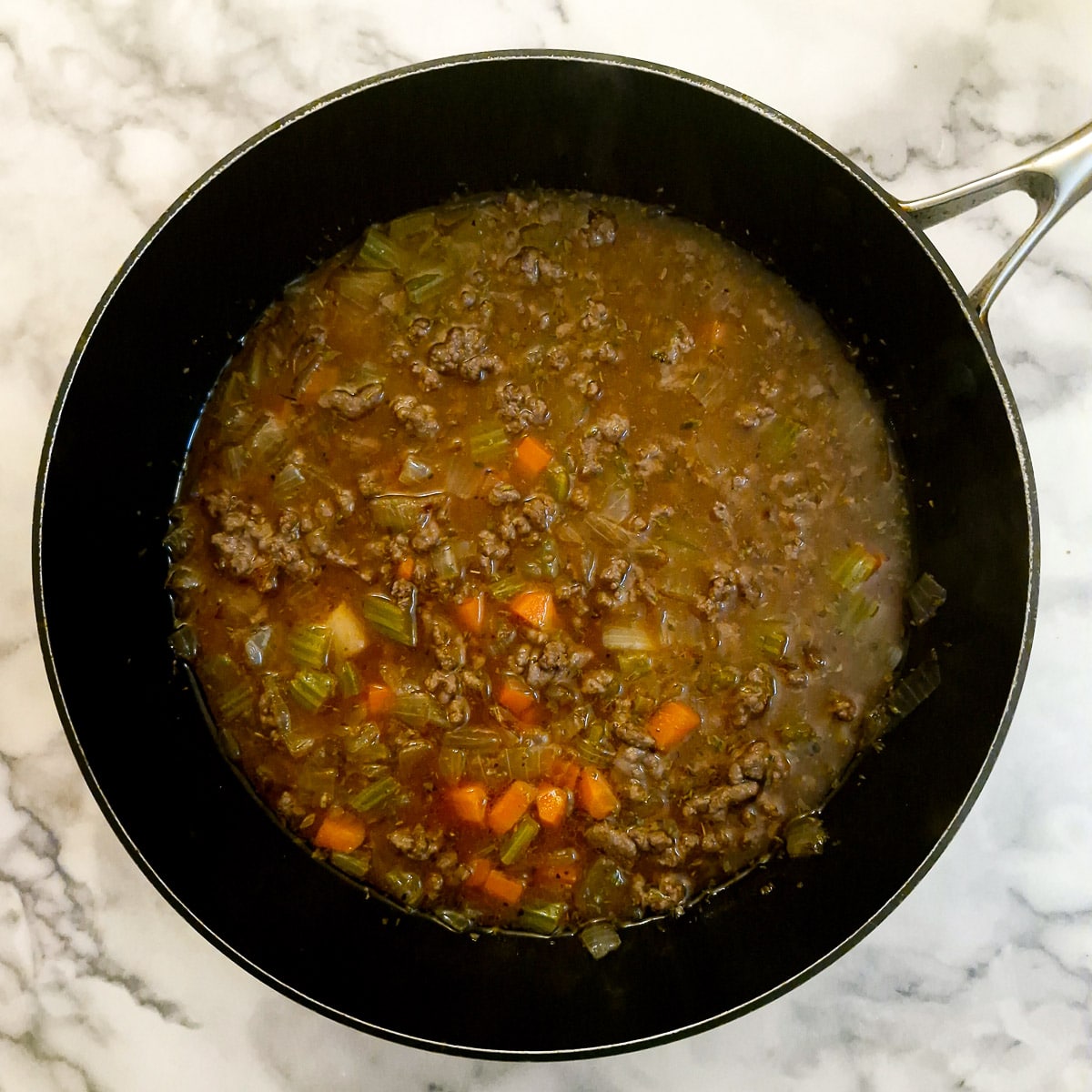 Stock added to beef and vegetables in a frying pan.